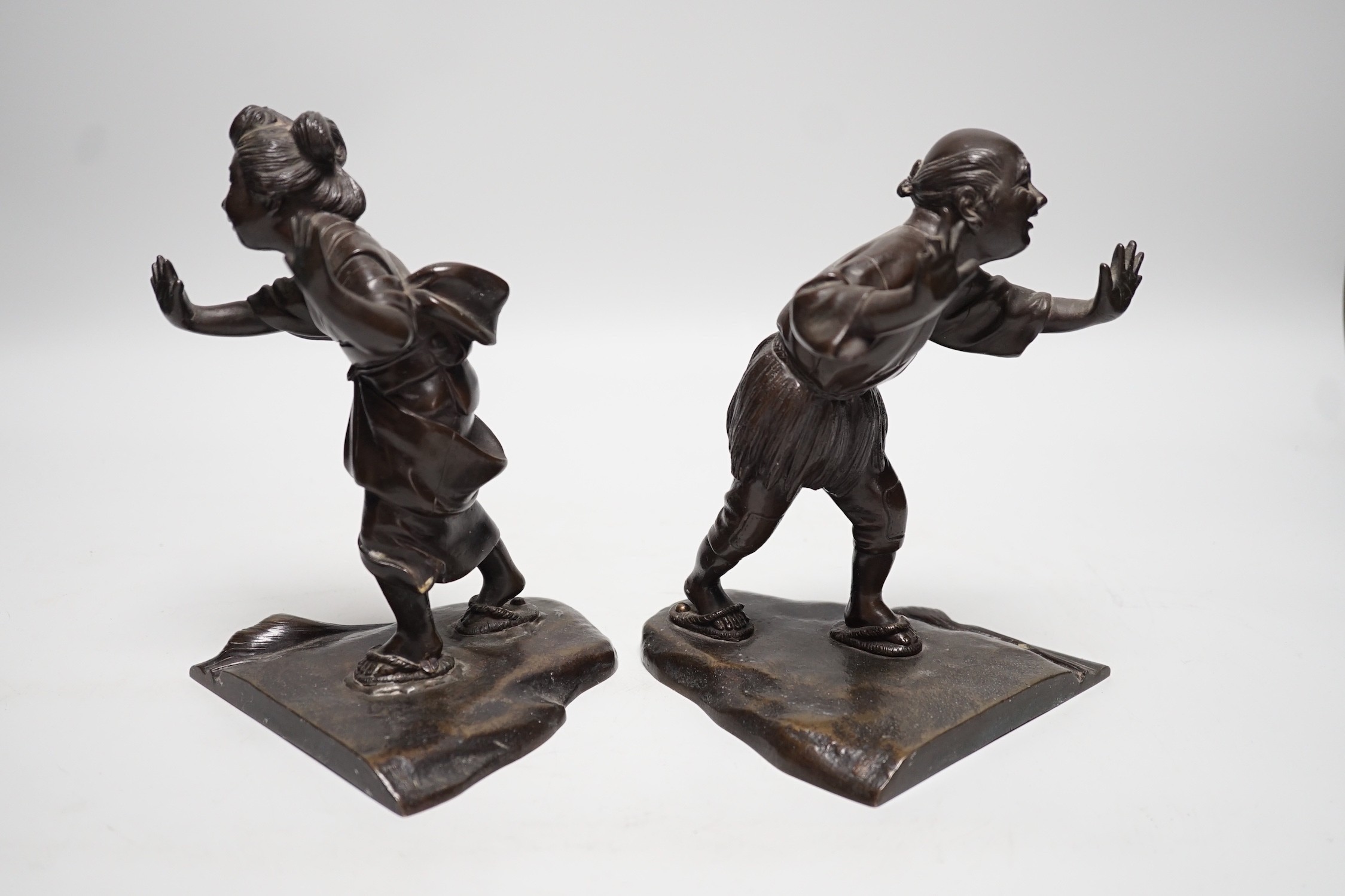 A pair of Japanese Meiji period bronze bookends modelled as a husband and wife pushing against each other, 18cm